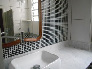 A bathroom with a white sink, a mirror with a wooden frame, and a tiled wall with a grid pattern. - Gohouse - Tonelero 403 (Rio de Janeiro)