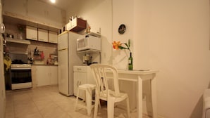 Una piccola cucina con mobili bianchi, un forno a microonde, un frigorifero, un tavolo da pranzo con due sedie e un vaso con fiori appeso al muro.