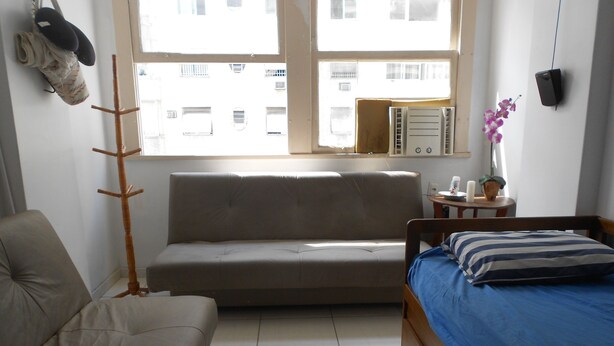 A room with a sofa, a bed, a wooden floor, a window, and a wall-mounted speaker. - Gohouse - Copacabana 402 (Rio de Janeiro)