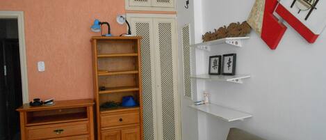 Una habitación con un aparador de madera, una lámpara azul, un estante blanco con fotografías enmarcadas y un adorno rojo y blanco en la pared.