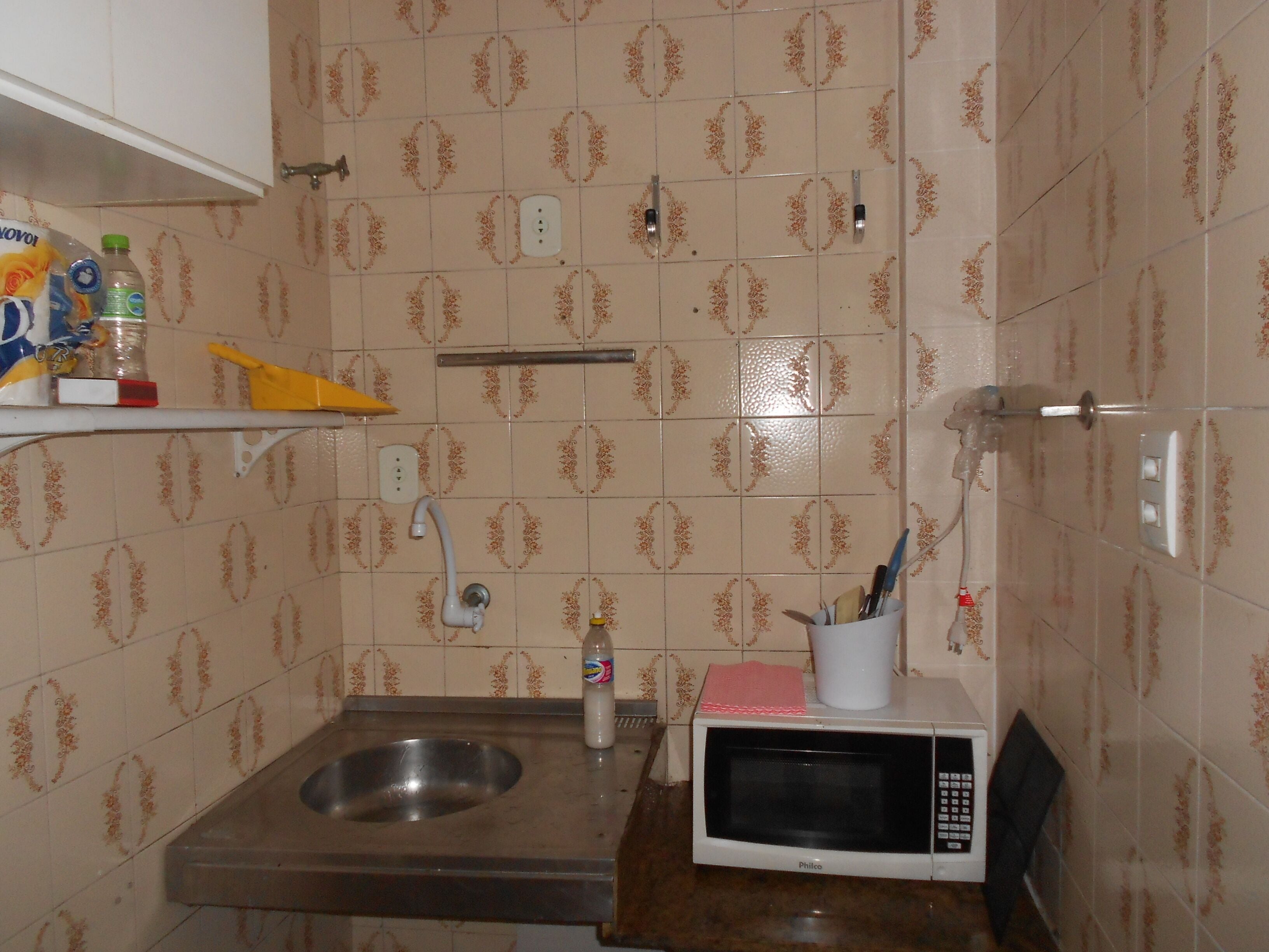 A small kitchenette with a sink, a microwave, and a shelf with kitchen items.