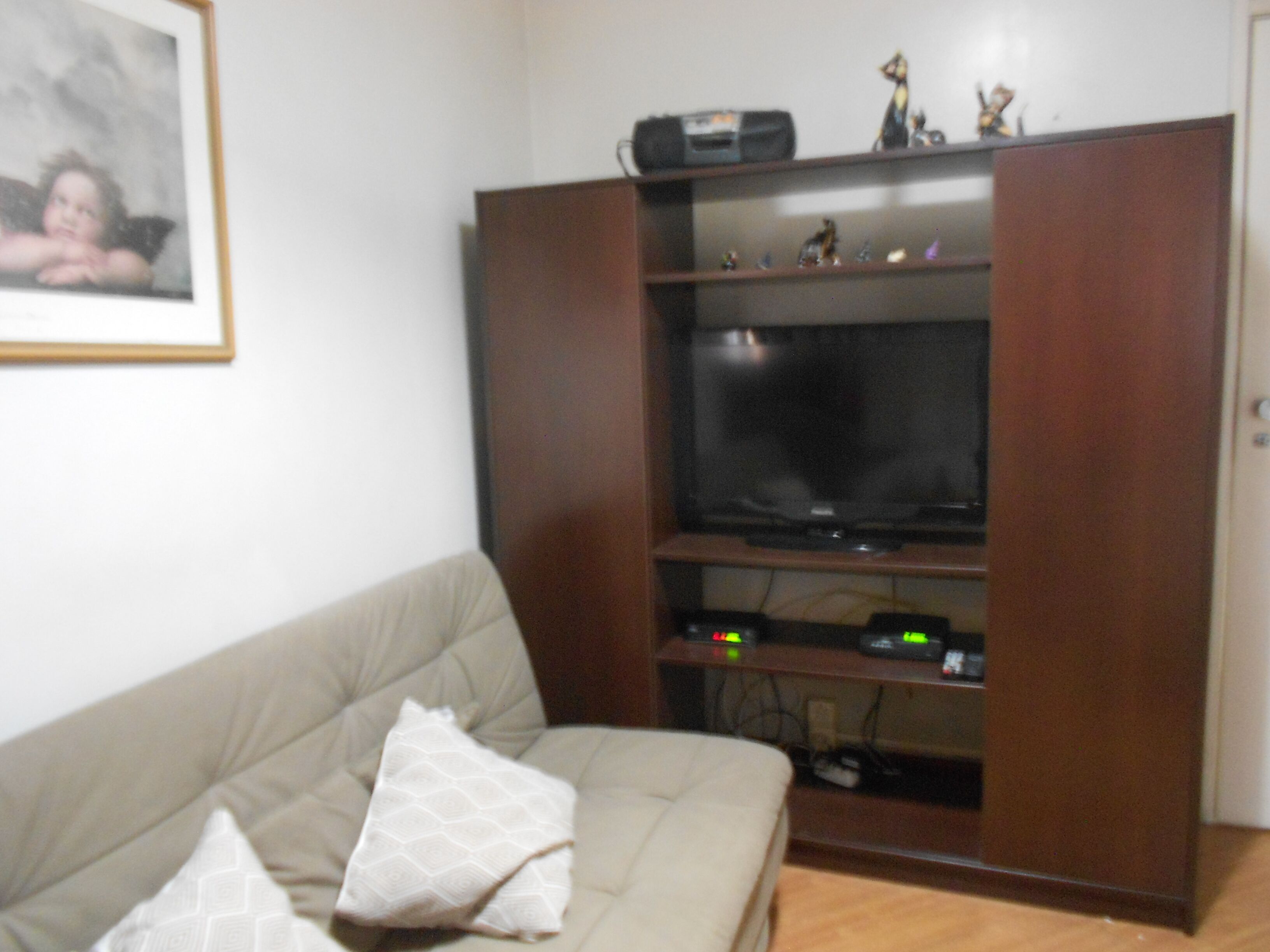 A living room with a beige sofa, a wooden entertainment unit with a flat-screen TV, and a framed picture on the wall.