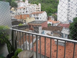 A view from a balcony with a chain-link fence, overlooking a residential area with terracotta-tiled roofs and white buildings.