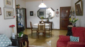 A living room with a dining area, a red sofa, and a wooden dining table. - Gohouse - Loureiro 102 (Rio de Janeiro)