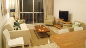 A living room with a sofa, coffee table, TV, and a large window with curtains. - Gohouse - Elizabeth 305 (Rio de Janeiro)