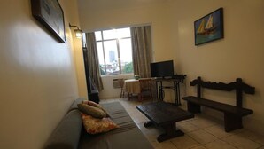 Un salón con sofá, mesa, banco, televisor y ventana con cortinas.