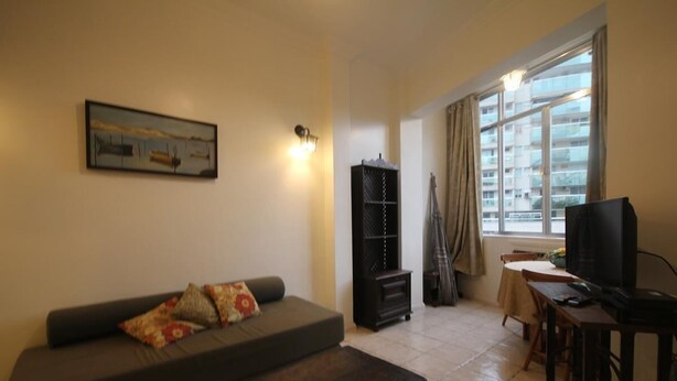 Una sala de estar con sofá, mesa de centro, televisor, estantería y ventana con cortinas.
