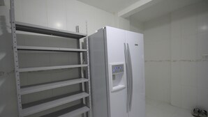 A white refrigerator with a water dispenser and a metal shelf unit in a kitchen. - Gohouse - Visconde 206 (Rio de Janeiro)