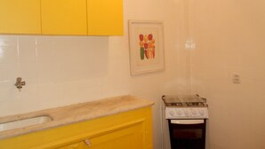 A small kitchen with yellow cabinets, a sink, and a stove. - Gohouse - Siqueira 1003 (Rio de Janeiro)