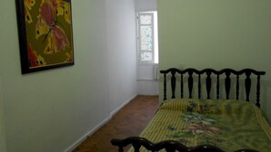 A bedroom with a wooden bed, a floral bedspread, and a painting on the wall. - Gohouse - Siqueira 1003 (Rio de Janeiro)
