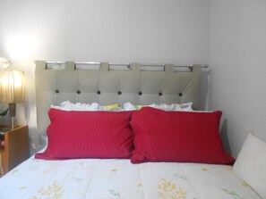 A bedroom with a bed, two red pillows, a white quilt, and a nightstand with a lamp.