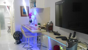 A modern living room with a flat-screen TV, a dining table with chairs, a standing fan, and a small kitchen area with a microwave. - Gohouse - Gustavo 404 (Rio de Janeiro)