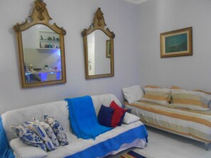 A room with a white sofa, a striped bed, two mirrors, and a framed picture on the wall.