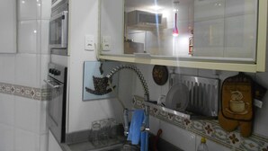 A kitchen with white tiles, a stainless steel oven, a microwave, and a hanging pot rack. - Gohouse - Gustavo 404 (Rio de Janeiro)