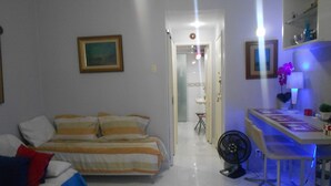 A bedroom with a bed, bedside table, and a desk with a chair. There is a fan on the floor next to the desk. - Gohouse - Gustavo 404 (Rio de Janeiro)