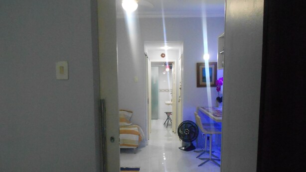 A hallway leading to a bedroom with a bed, a fan, and a small table. - Gohouse - Gustavo 404 (Rio de Janeiro)