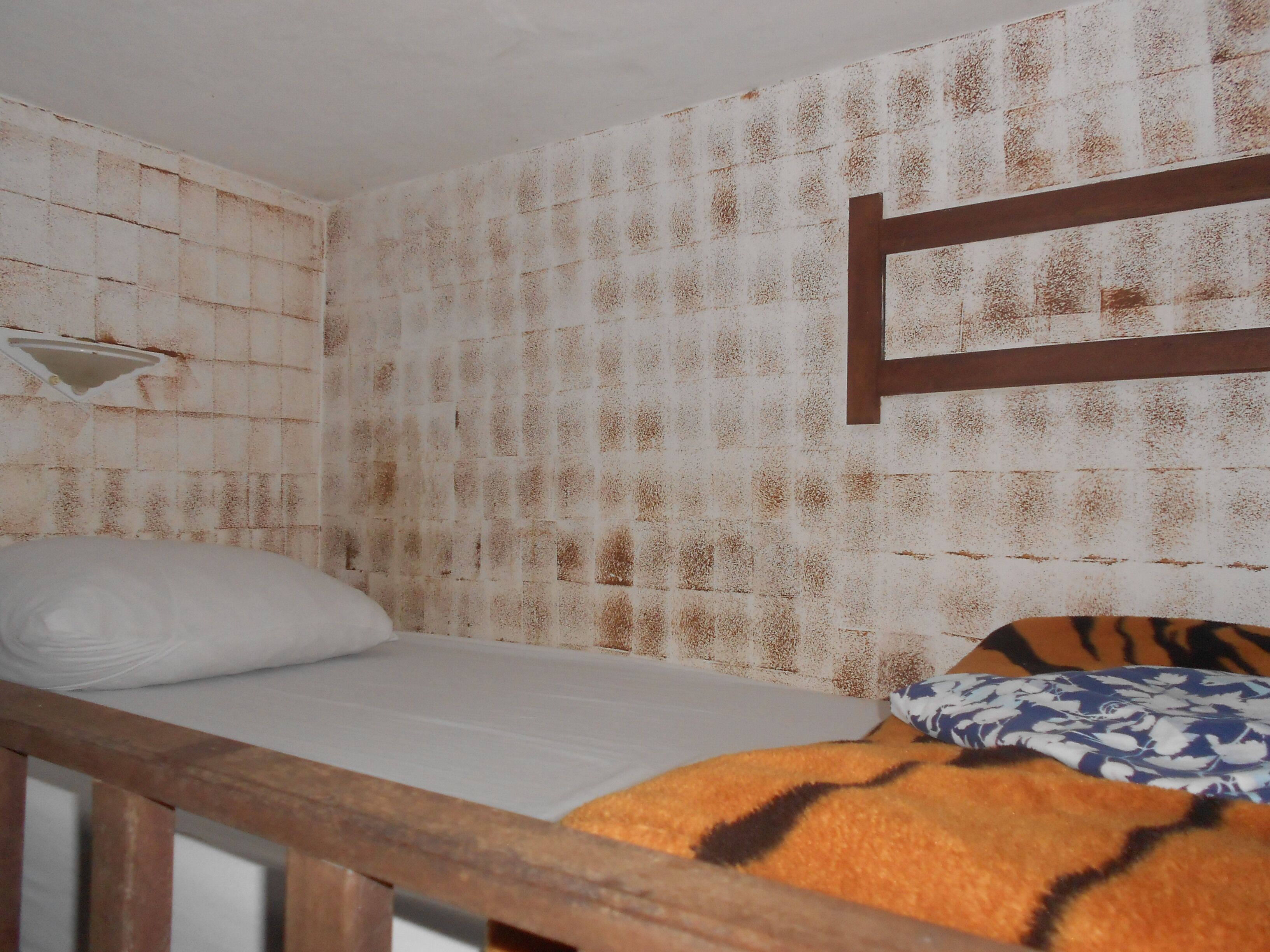 Un letto singolo con materasso bianco e testiera in legno, un cuscino bianco e una coperta fantasia.