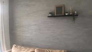 A beige sofa against a grey wall with a small shelf above it.