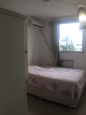 A bedroom with a bed, a window with curtains, an air conditioning unit, and a radiator.