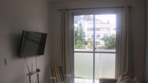 A living room with a sofa, a TV mounted on the wall, a chair, and a window with curtains.