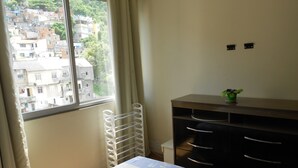 A bedroom with a bed, a dresser, a radiator, and a window with a view of a cityscape. - Gohouse - Siqueira 703 (Rio de Janeiro)