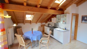 A cozy kitchen with wooden beams, a dining area with wicker chairs, and a small island with a sink. - Solinda (Garmisch-Partenkirchen)