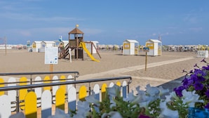 Una playa con un parque infantil, cabañas de playa y una torre de salvavidas.