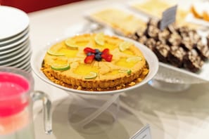 A dessert display with a pie topped with fruit and lime slices, accompanied by other desserts and a glass pitcher.