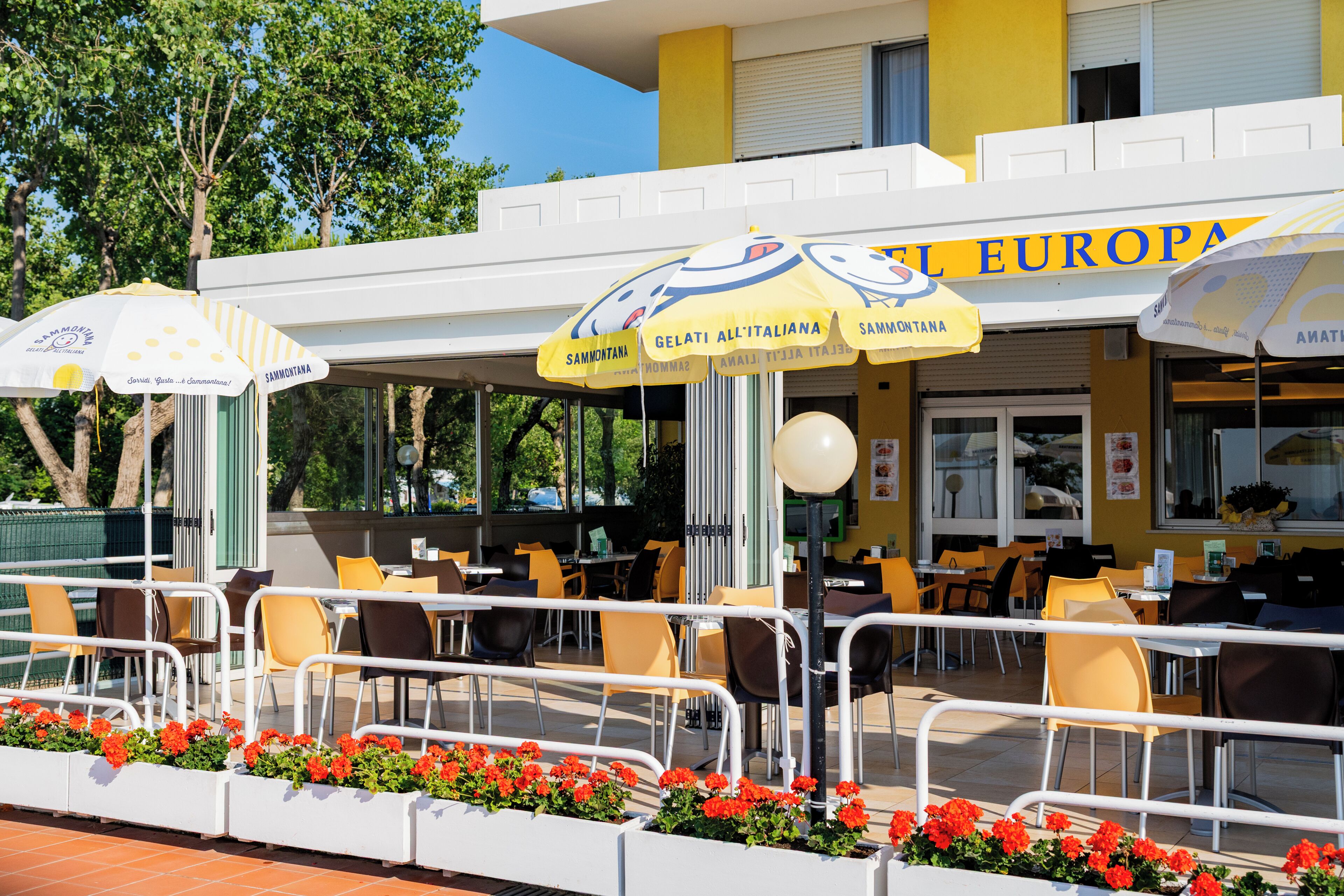 An outdoor cafe with yellow and white umbrellas, outdoor seating, and a yellow building with 'EL EUROPA' signage.