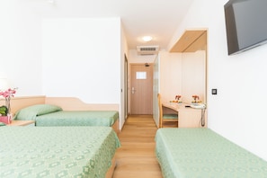 A hotel room with two single beds, a desk with a chair, a flat-screen TV mounted on the wall, and a small table with a telephone.