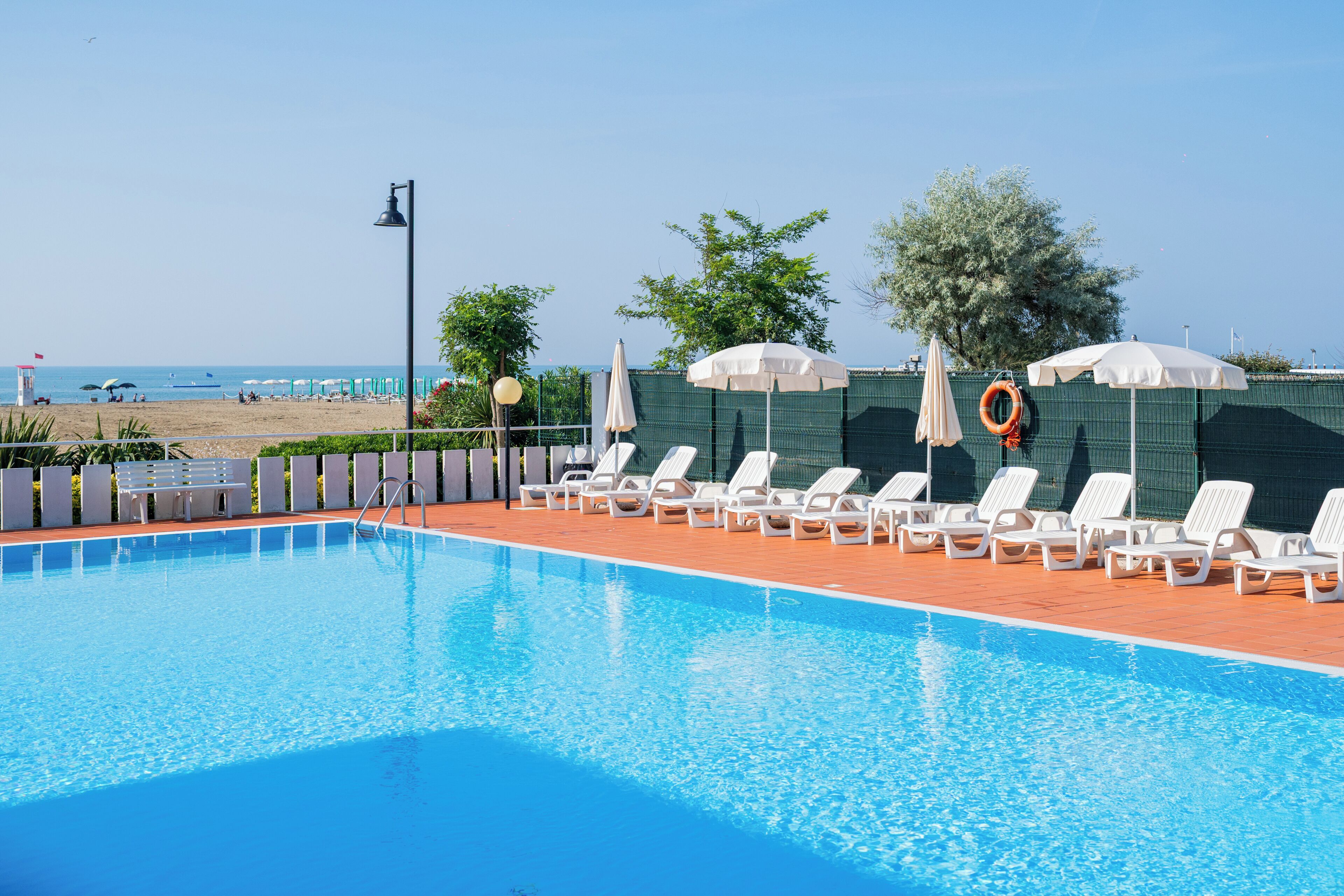 Une piscine avec des chaises longues et des parasols, un banc et une bouée de sauvetage.