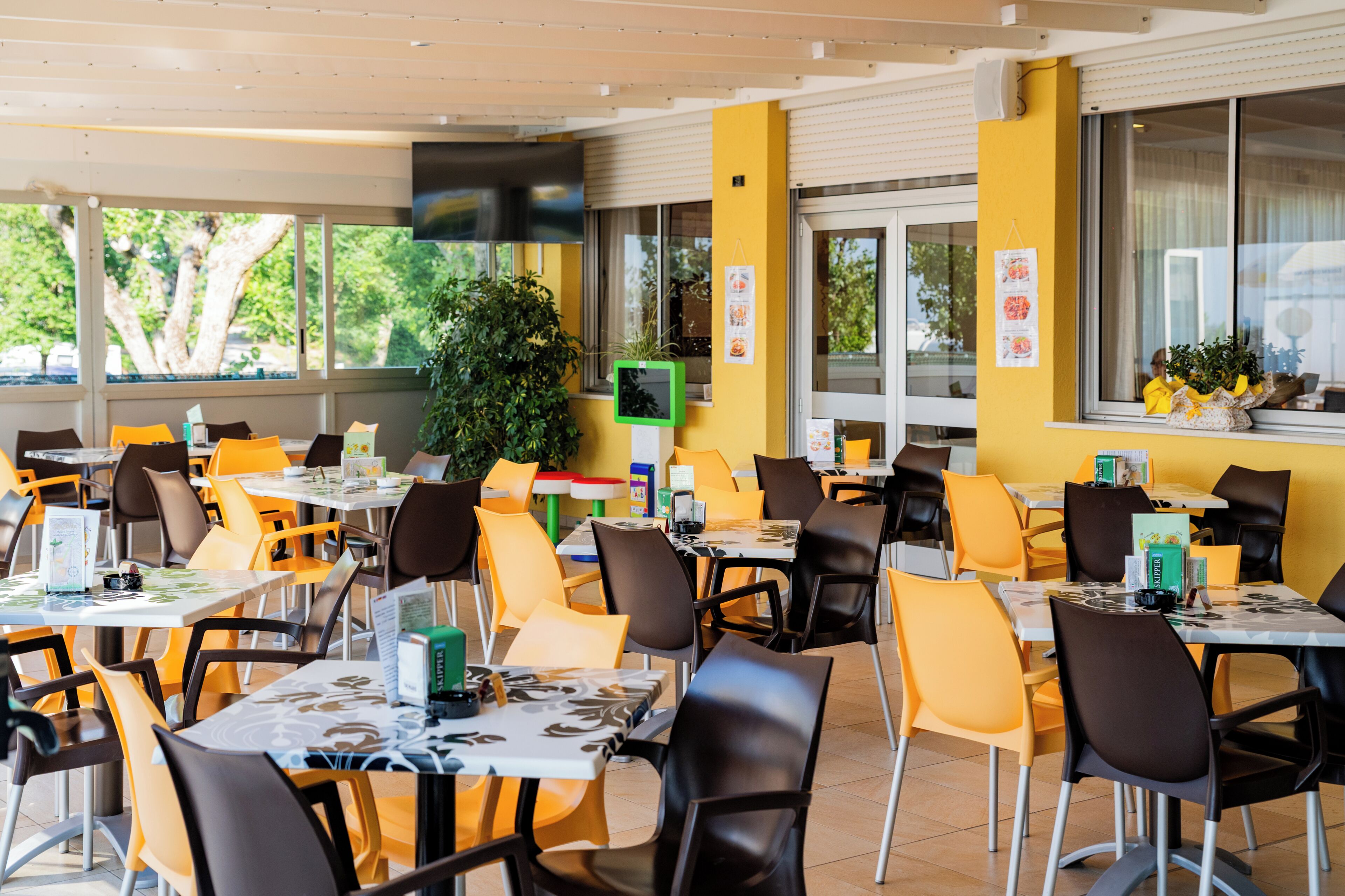 A restaurant with yellow walls, multiple tables and chairs, and large windows.