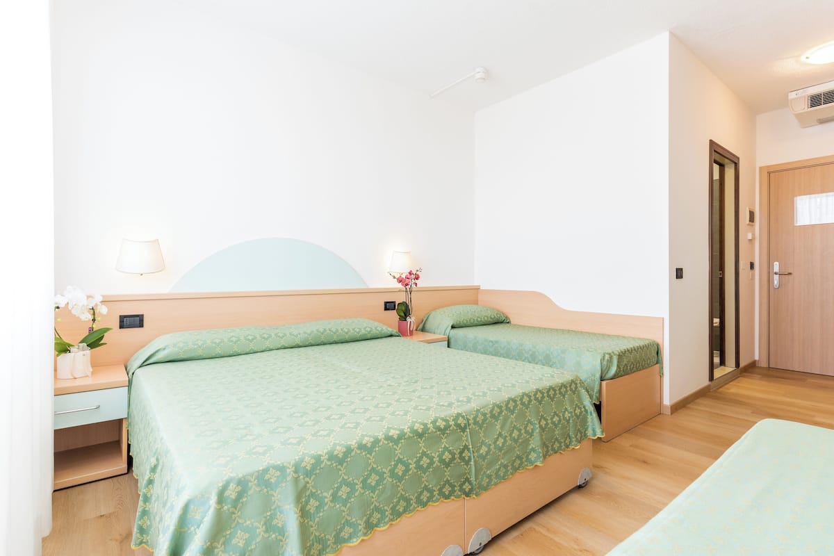 A hotel room with two beds, a bedside table with a lamp, a small desk, and a mirror.
