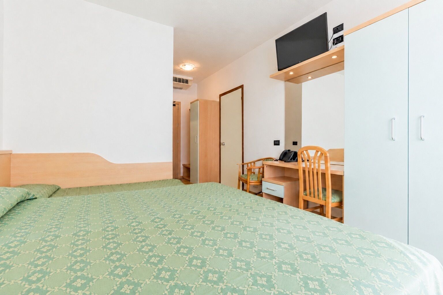 Ein Schlafzimmer mit Bett, Schreibtisch, Stuhl, Kleiderschrank und Fernseher.