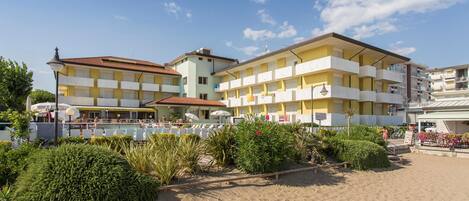 Ein Hotel an der Küste mit mehreren Balkonen, ein Sandstrand davor und ein klarer Himmel.