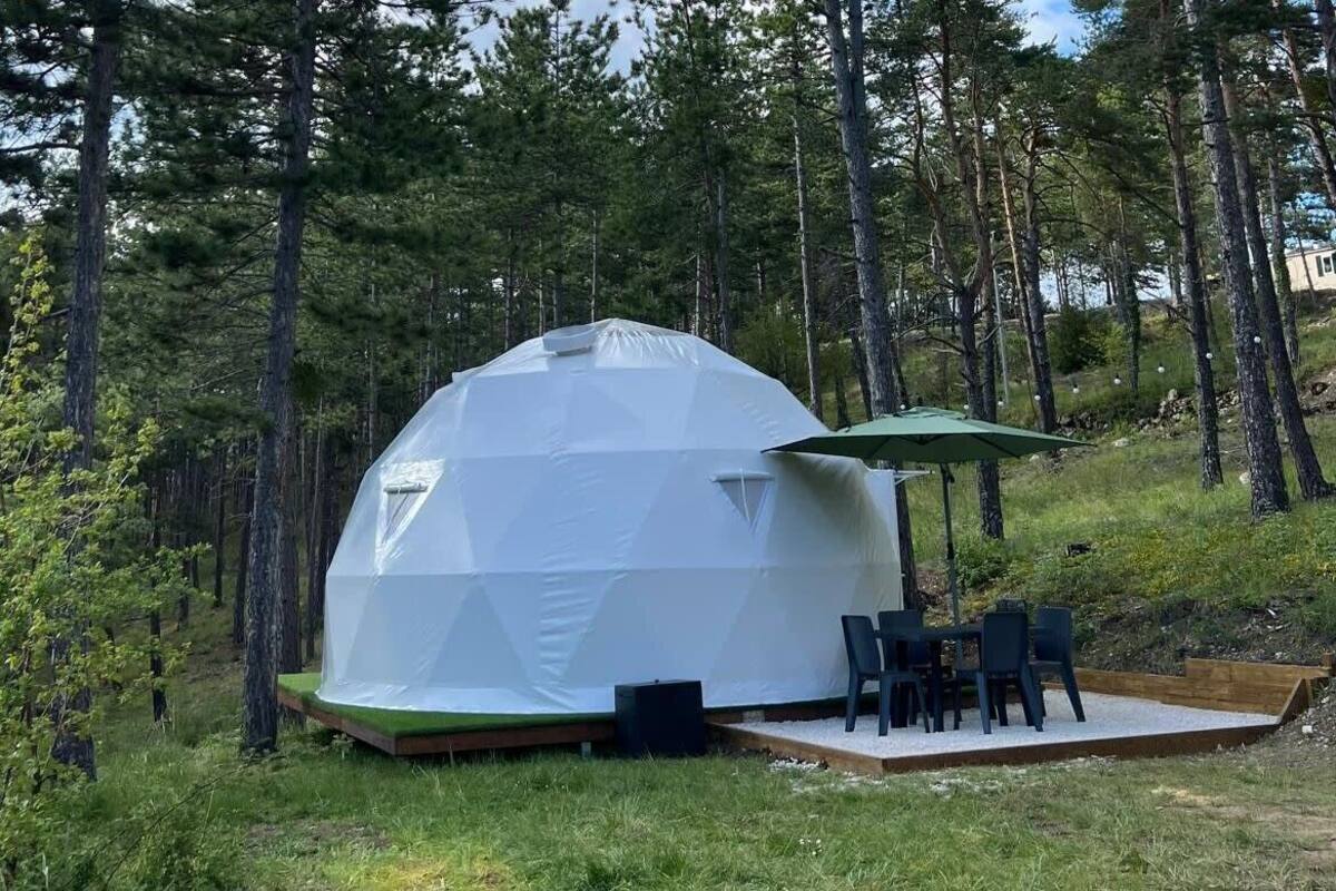 Een geodetische koepeltent met een tafel en stoelen buiten, omringd door bomen.