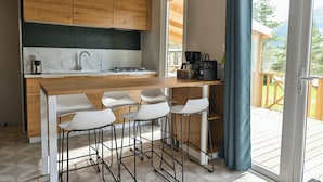 A modern kitchen with wooden cabinets, a marble backsplash, a gas stove, and a bar area with stools. - Camping RCN Les Collines de Castellane (La Garde)