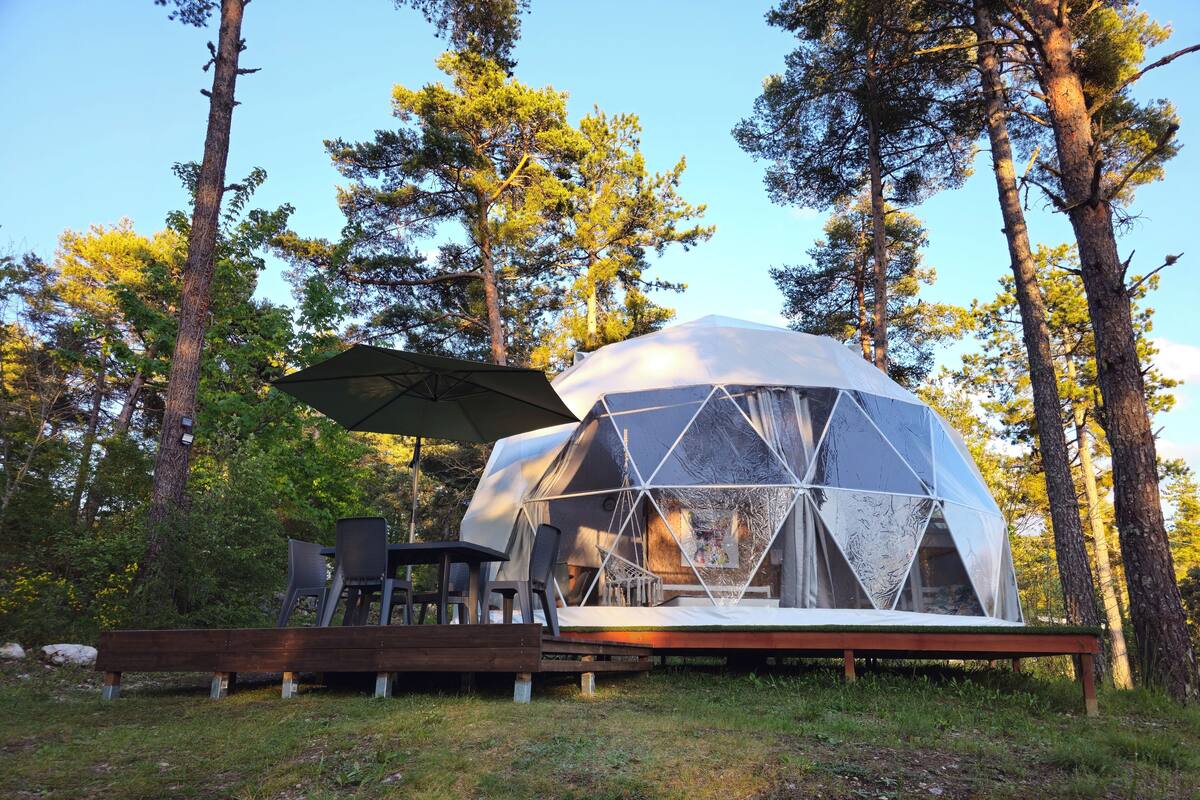 Een geodetische koepelstructuur met een terras, zitplaatsen buiten en een grote parasol.