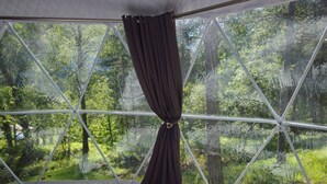 A tent-style room with a bed, a colorful woven rug, and a view of a forest through a large window. - Camping RCN Les Collines de Castellane (La Garde)