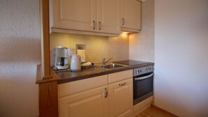 A small kitchen with light-colored cabinets, a sink, a stove, and a coffee maker. - Wettersteinblick (Garmisch-Partenkirchen)