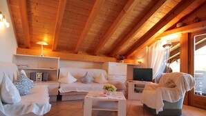Un salon chaleureux avec un plafond en bois, un canapé, un fauteuil, une table basse et un téléviseur.