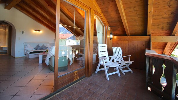 Un intérieur en bois avec un balcon, des chaises blanches et un canapé.