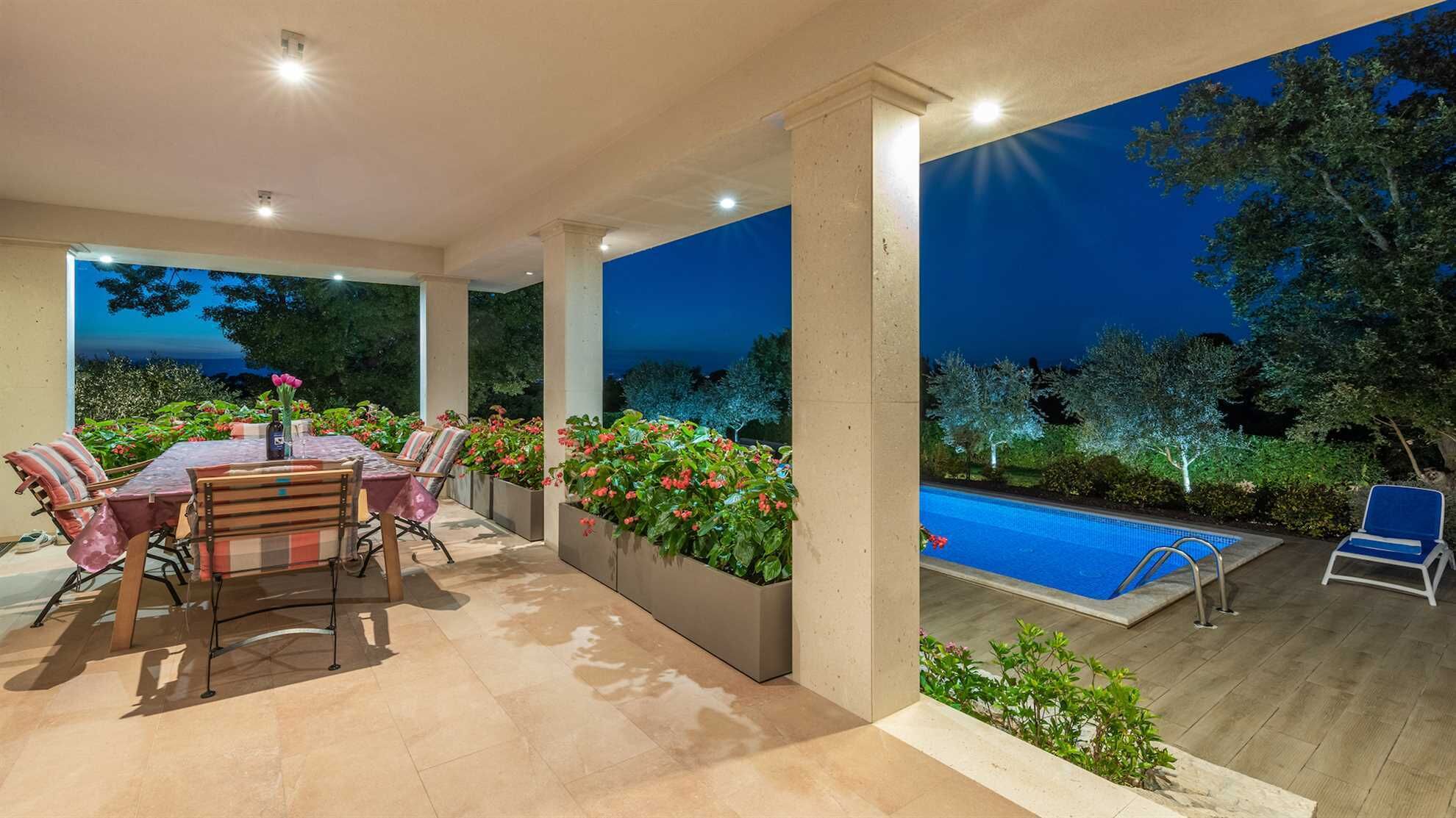 An outdoor patio with a pool, surrounded by plants and a view of the night sky.