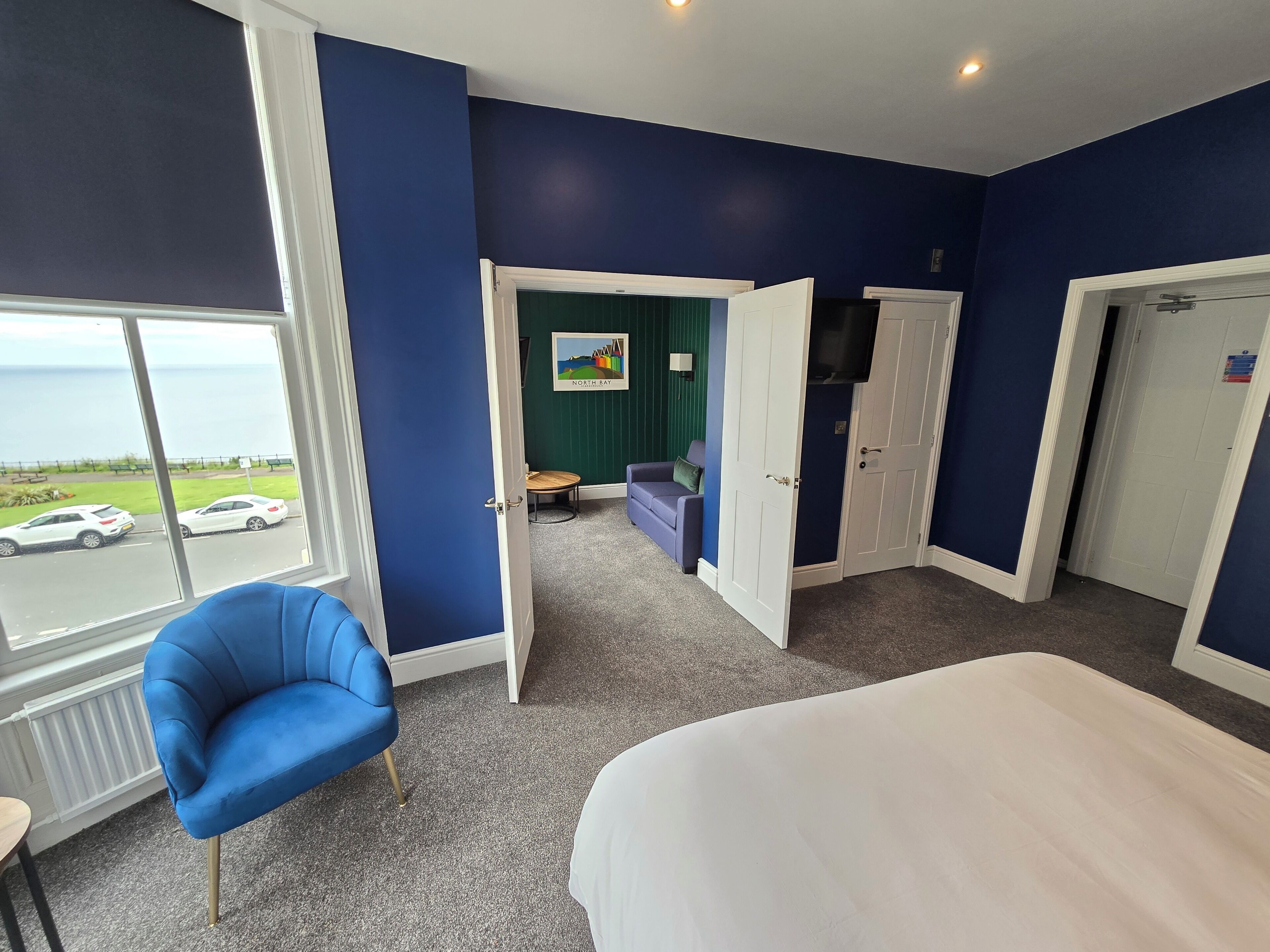 A hotel room with a large bed, a blue armchair, a small table, and a view of the sea through a large window.