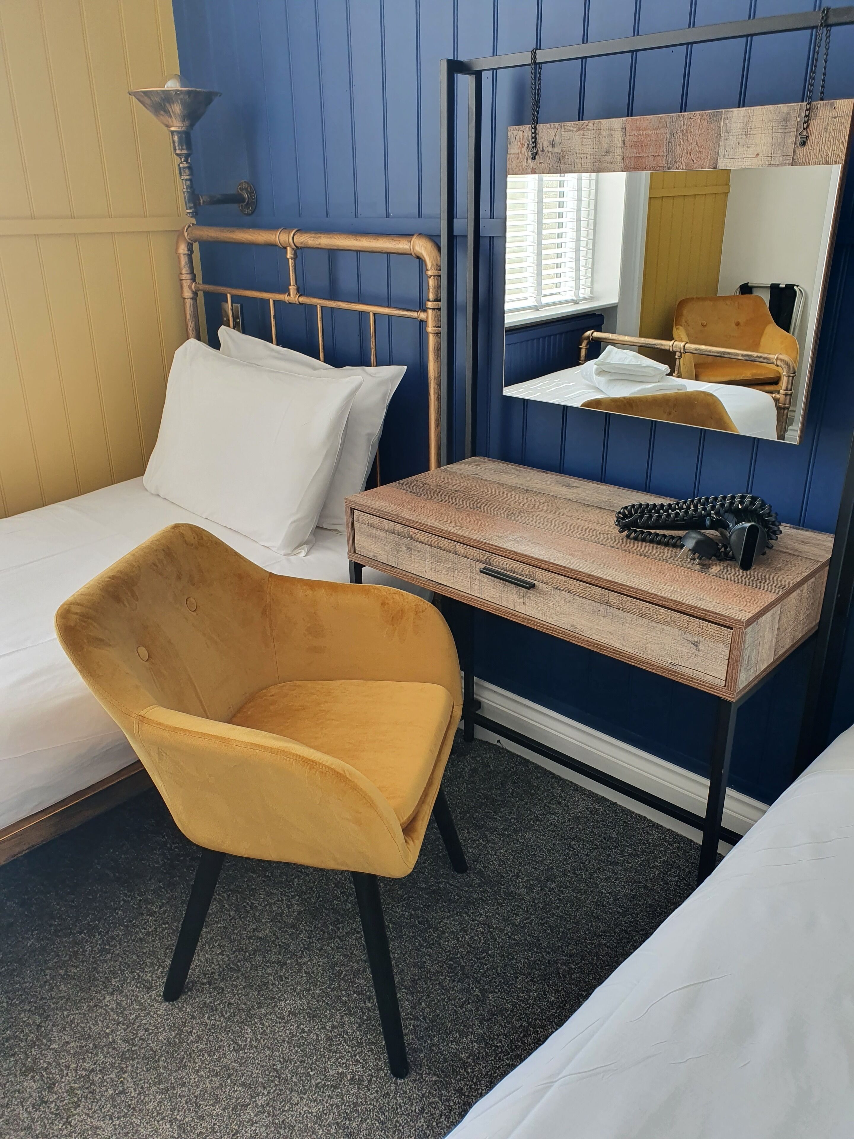 Una habitación de hotel con una cama, una silla, una mesita de noche con una lámpara y un espejo.