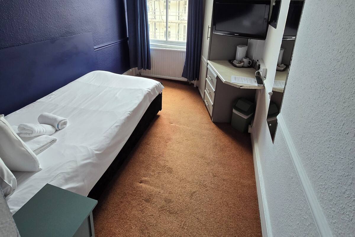 Hotellihuone, jossa on sänky, työpöytä, tuoli, televisio ja ikkuna, jossa on verhot.