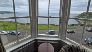 A bay view from a corner room with a view of the sea, parking area, and grassy landscape. - Delmont Hotel (Scarborough)
