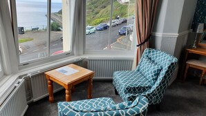 A corner room with a bay window overlooking a parking area and a coastal view. - Delmont Hotel (Scarborough)