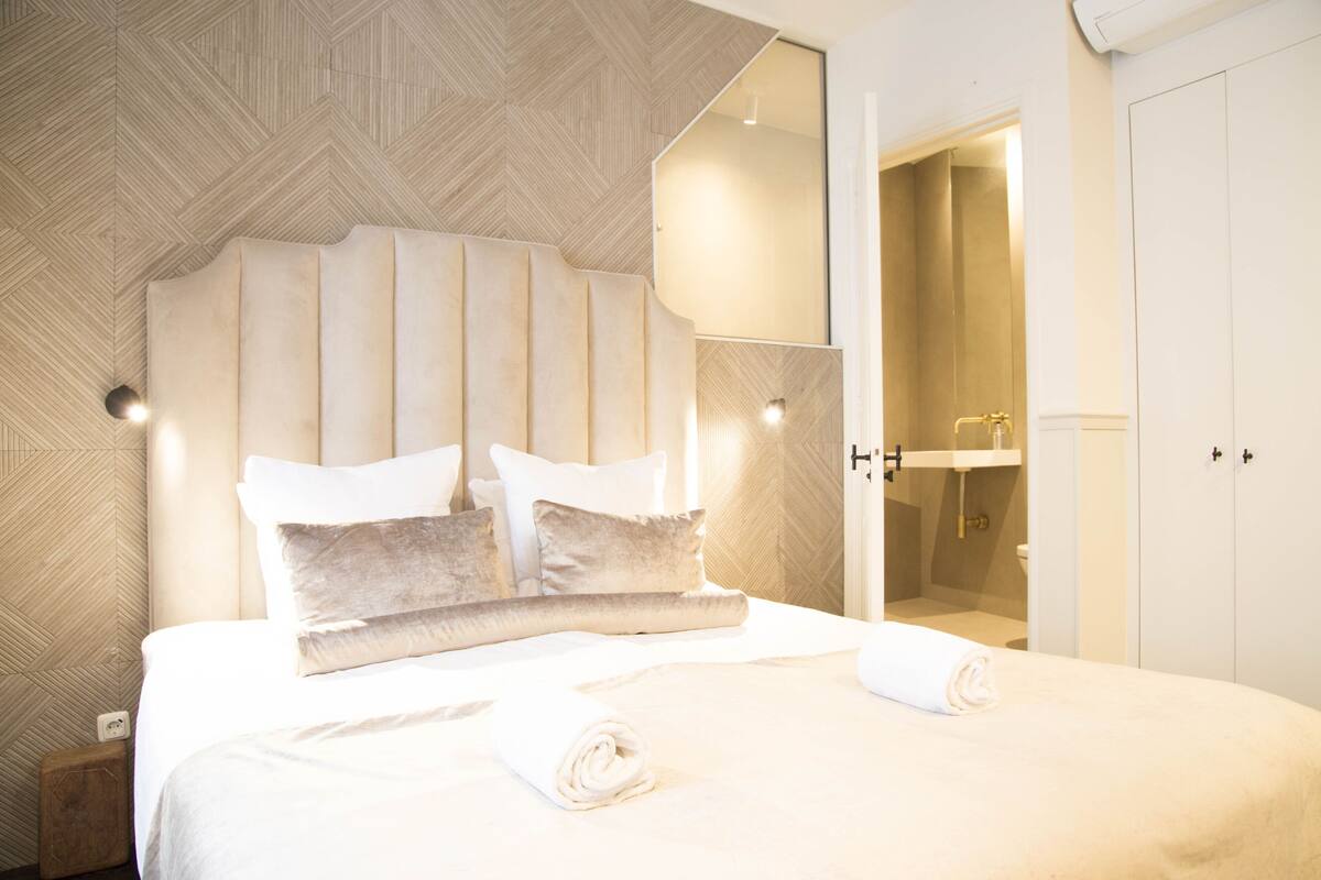 A hotel room with a large bed, a headboard, and a bathroom visible through an open door.