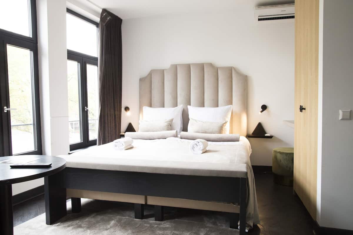 A modern hotel room with a large bed, bedside lamps, a small round table, and a view through the window.